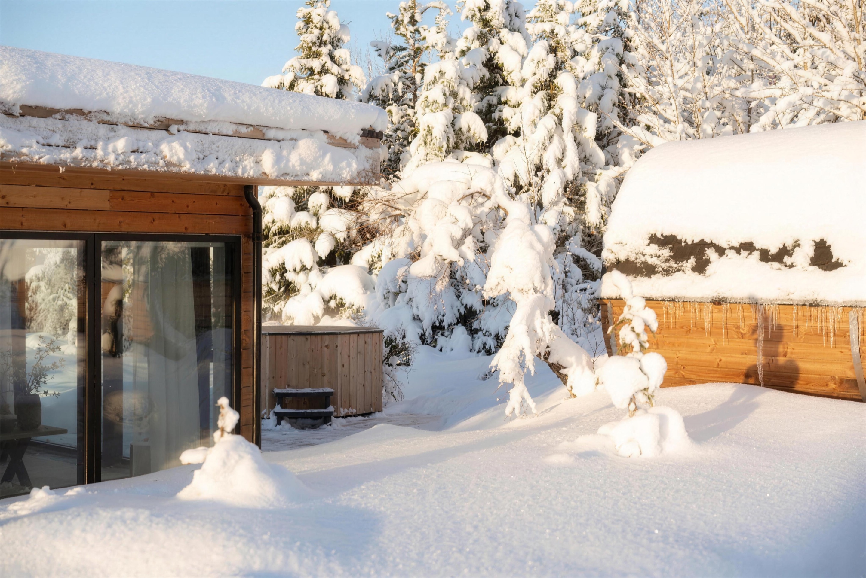 Deep snow around the glass house at midwinter, low sun on the drifts and icicles hanging from the sauna roof