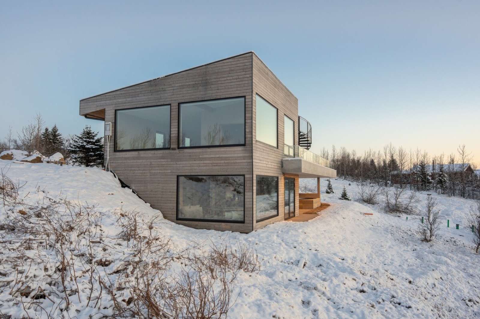 The timber clad house on the ridge under snow, low winter light on the glass